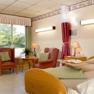 A well-furnished hospital room featuring a bed, seating area, and natural light from the window.