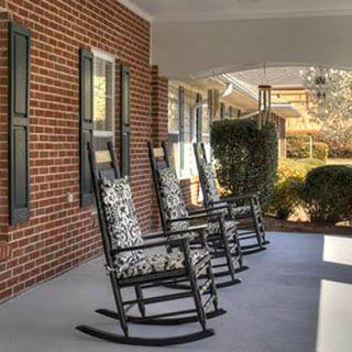 A cozy front porch with rocking chairs lined up against a brick wall.