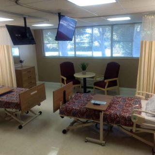 A hospital room with two beds, chairs, and televisions.