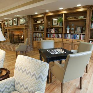 A cozy library with a fireplace, bookshelves, and a seating area featuring a chess table.
