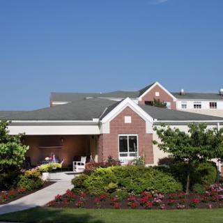 A charming residential building surrounded by lush gardens and a clear blue sky.