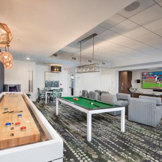 A modern game room featuring a pool table, shuffleboard, and comfortable seating area with a large television.