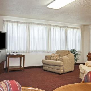A cozy living room with sofas, armchairs, a television, and large windows with blinds.