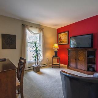 A cozy living room with a red accent wall, featuring a TV, desk, and comfortable seating.