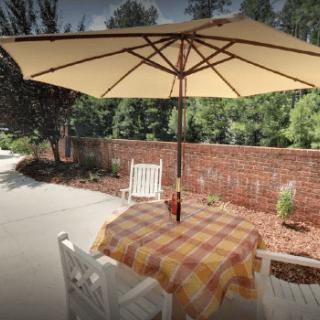 A cozy outdoor patio setup with a table, chairs, and a large umbrella providing shade.