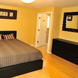A neatly arranged bedroom with a bed, dresser, and mirror on a wooden floor.