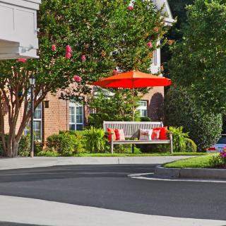 A welcoming bench under a red umbrella outside a residential building, surrounded by greenery.