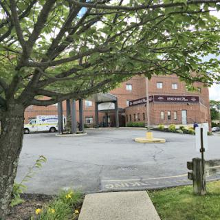 A view of a hospital with a parking area, surrounded by greenery.
