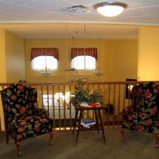 A cozy living room seating area with floral patterned chairs and a central wooden table, illuminated by ceiling lights.