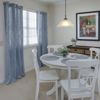 A cozy dining room with a round white table and chairs, blue curtains, and illuminated by a hanging lamp.