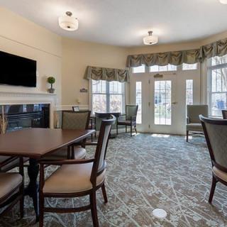 A cozy living room with tables, chairs, a television, and a fireplace near large windows.