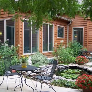 A cozy garden patio with a small pond surrounded by lush greenery and outdoor seating.