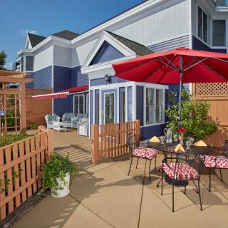A cozy outdoor patio with red umbrellas and seating, set against a blue residential building.