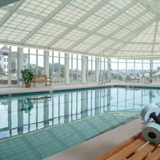 A serene indoor swimming pool with a glass ceiling and modern gym equipment nearby.