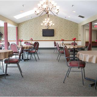 A spacious dining area featuring tables and chairs, adorned with a decorative chandelier and wallpaper.
