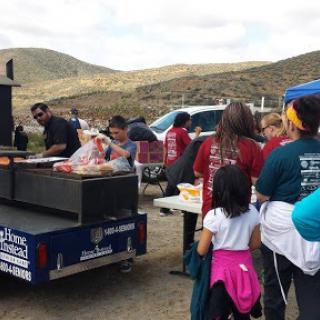 A community cookout with volunteers serving food from a food truck in a scenic outdoor location.
