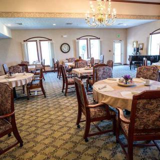 A spacious dining area with neatly arranged tables and chairs, featuring a chandelier and grand piano.