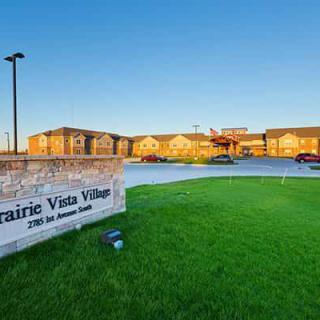 A view of Prairie Vista Village featuring a well-maintained lawn and a welcoming entrance.
