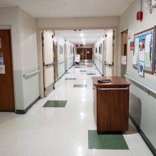 A view of the quiet hallway in a hospital, featuring multiple doors and a trash receptacle.