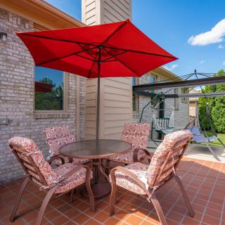 A cozy patio setup featuring a red umbrella, round table, and cushioned chairs against a brick wall on a sunny day.