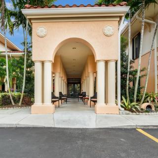 An elegant archway with columns leads to the entrance of a tropical building, surrounded by lush plants.