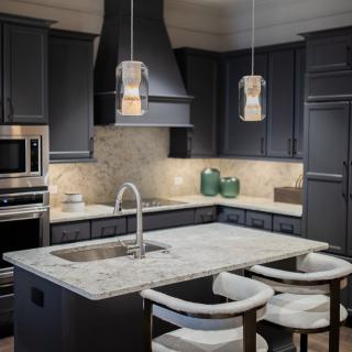 A modern kitchen with dark cabinetry, a marble countertop island, and stylish pendant lighting.