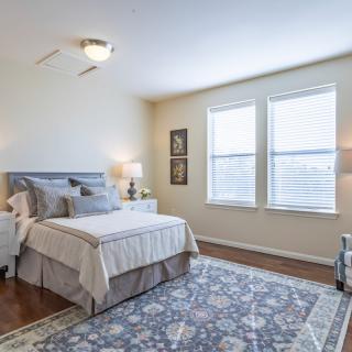 A cozy bedroom with a neatly made bed, stylish rug, and ample natural light coming through the windows.