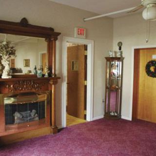 A cozy interior features a decorative fireplace with an ornate mirror, plush carpet, and elegant furnishings.
