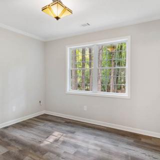 An empty room with wood flooring, white walls, and a large window letting in natural light.