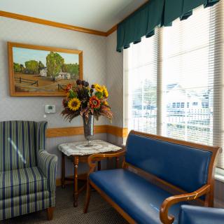 A cozy waiting room with comfortable seating, a vase of flowers, and a scenic painting.