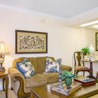 A cozy living room featuring a comfortable sofa with decorative cushions, artwork on the wall, and a wooden coffee table adorned with accessories.