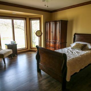 A cozy bedroom with a single bed, wooden wardrobe, and large window allowing natural light.