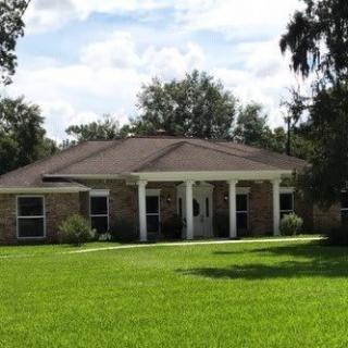 A brick house with a large lawn and front porch under a clear sky.