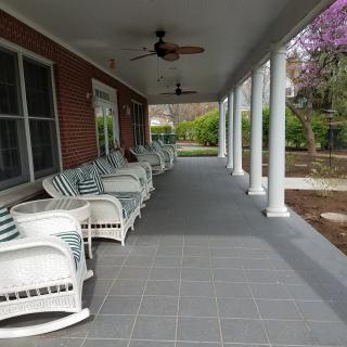 A covered porch with white chairs and columns, offering a peaceful outdoor seating area.