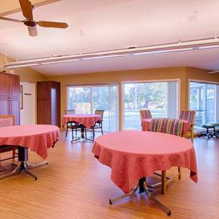A cozy dining area with tables covered in pink tablecloths, surrounded by large windows and a ceiling fan.
