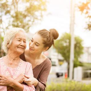 A young woman affectionately embraces an elderly woman in a serene outdoor setting.