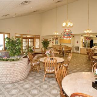 A cozy cafe interior featuring wooden tables and chairs, indoor plants, and warm lighting.