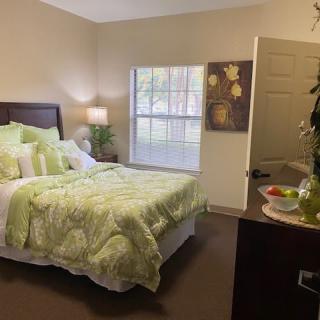 A cozy bedroom with a neatly made bed, featuring green bedding and soft lighting from a bedside lamp.