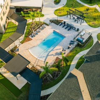 Aerial view of a residential outdoor area featuring a swimming pool surrounded by landscaped pathways and leisure spaces.