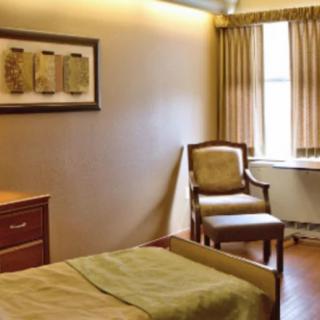 A cozy bedroom featuring a bed, chair, window with curtains, and wall artwork.