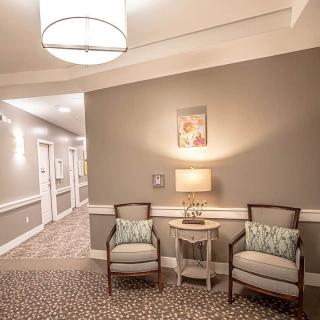 A cozy hallway with two chairs, a side table, and a lamp under soft ambient lighting.
