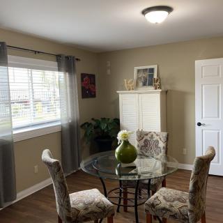 A cozy dining room featuring a glass-top table with ornate chairs, complemented by soft lighting and neutral decor.