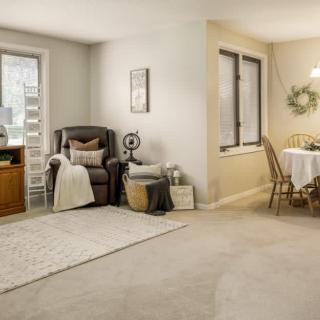 A cozy living room with an adjacent dining area, featuring an armchair, carpet, and a round table with chairs.