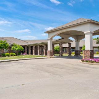 A welcoming entrance to a residential building, featuring well-maintained landscaping and a clear blue sky.