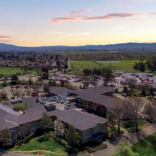 Aerial view of a residential area surrounded by greenery and mountains at sunset.