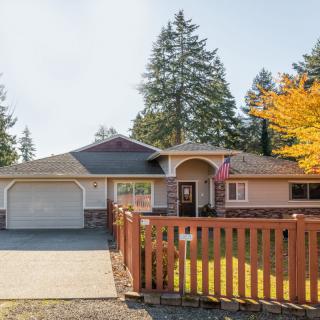 A suburban house with a fenced yard and driveway, surrounded by trees.