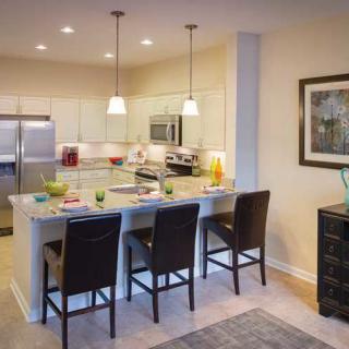 A modern kitchen with a large island, bar stools, stainless steel appliances, and pendant lighting.