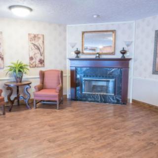 A cozy living room featuring a fireplace, two chairs, a side table with a plant, and wooden flooring.