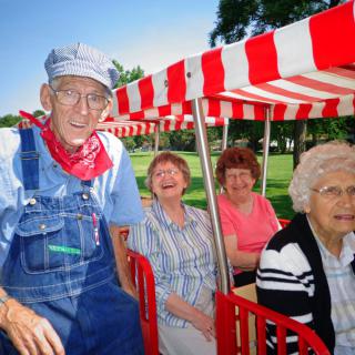 A group of elderly individuals enjoying an outdoor train ride under a red and white striped awning.