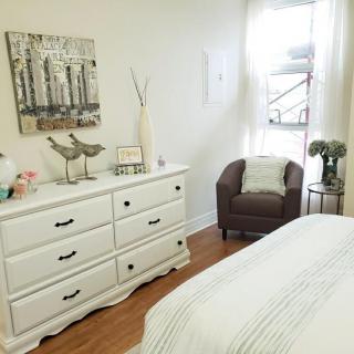 A bright and airy bedroom featuring a white dresser, cozy armchair, and minimalist decor.